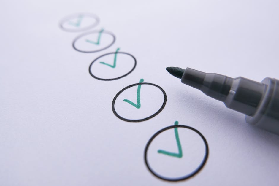 Close-up image of a white paper with six checkboxes arranged vertically, all marked with green check marks inside black circles. To the right of the paper, a grey marker with a black tip is positioned